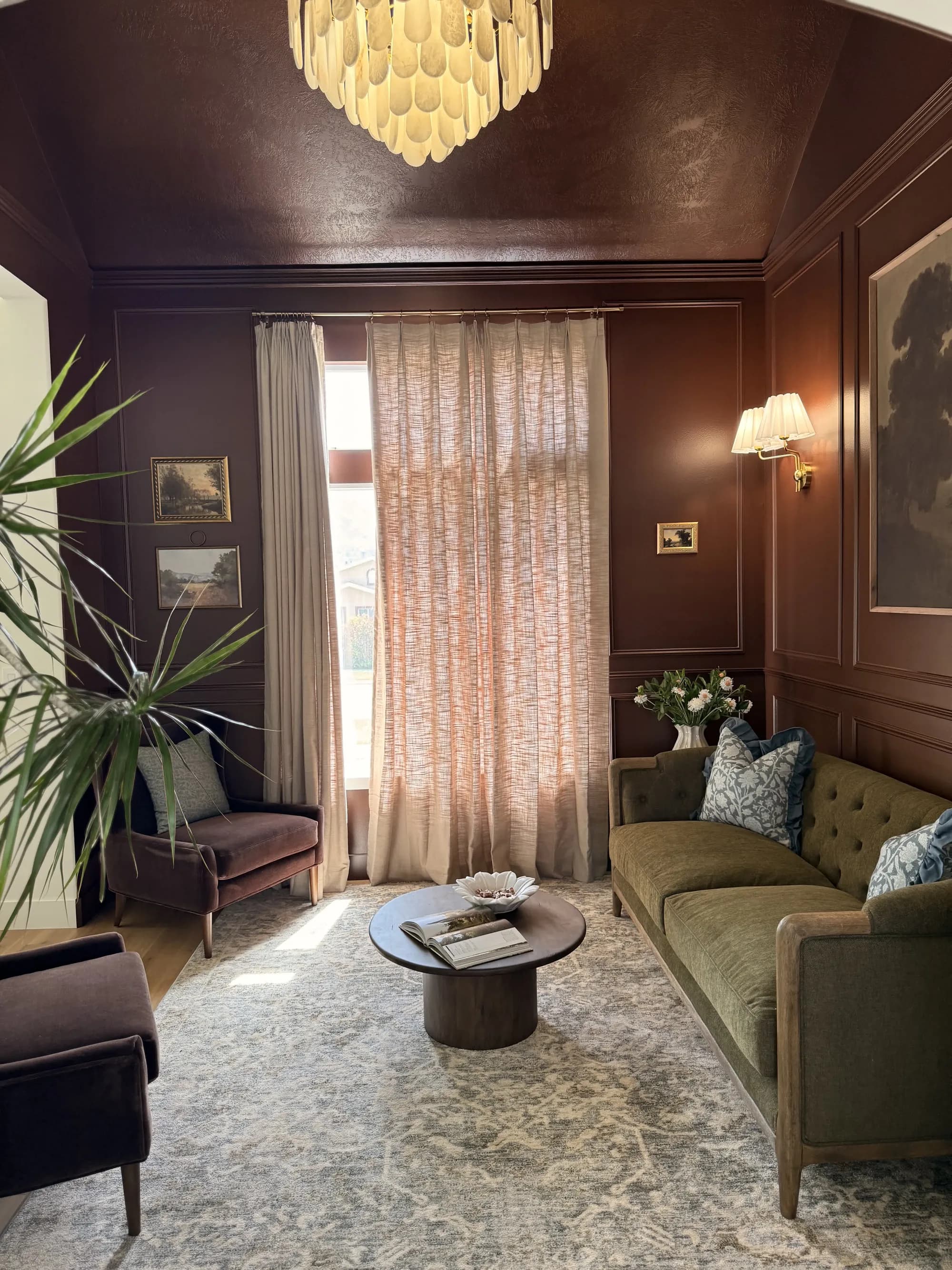 Terracotta paneled sitting room with picture molding, landscape art, and green velvet sofa by BK Toolbox